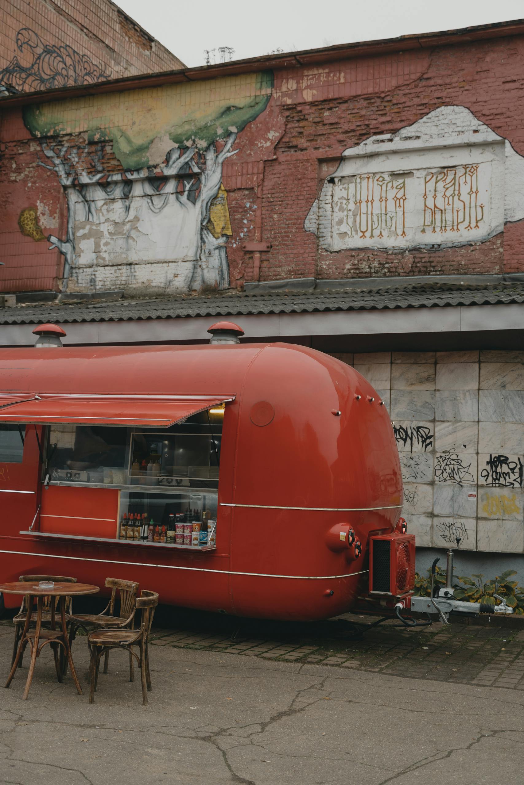 A retro red food truck parked in front of an urban graffiti mural with a rustic table setting.